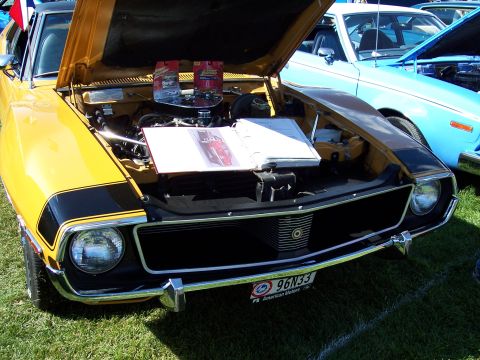 1972 Ford Ranchero - A yellow 1970 AMC Gremlin is displayed with its hood open, revealing the engine and a booklet on display.