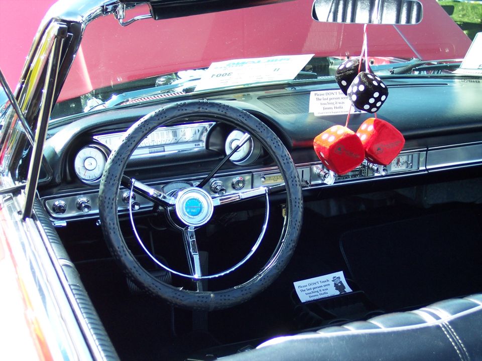 Interior of a classic car with a steering wheel, dashboard, and red fuzzy dice hanging from the rearview mirror