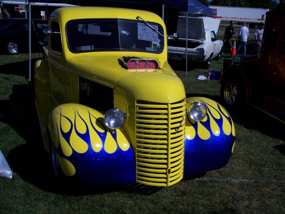 Yellow hot rod truck with blue and yellow flame decals on fenders, prominent grille, and hood scoop