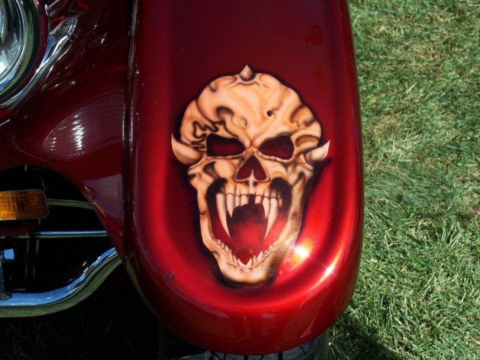 Red fender with airbrushed skull graphic, showing fangs and menacing eyes