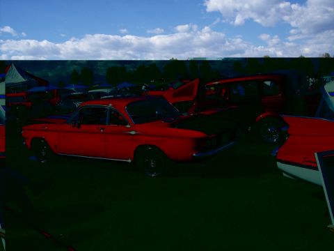 1972 Ford Ranchero - A red coupe with black accents is parked on a grassy field under a blue sky with clouds.