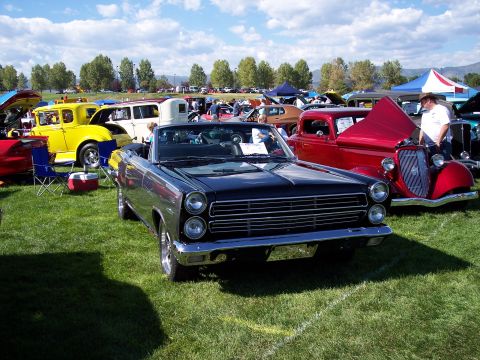1972 Ford Ranchero - A black convertible is parked on grass at an outdoor car show with other vehicles and attendees.