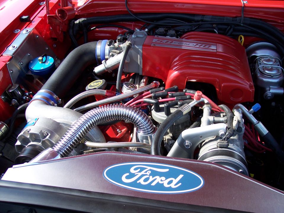Close-up of a red Ford 5.0 HO engine with chrome intake piping and a Ford oval logo