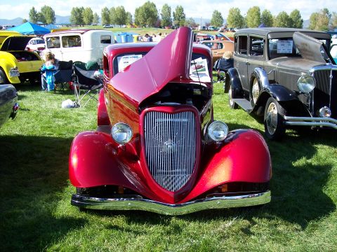 1972 Ford Ranchero - A shiny red hot rod is displayed with its hood open at an outdoor car show, parked next to another classic vehicle.