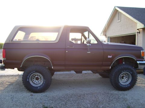 1990 Ford Bronco - This lifted Ford Bronco is parked in front of a residential garage during the day.
