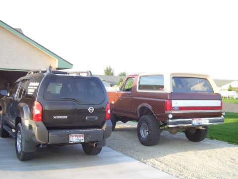 1990 Ford Bronco - A maroon 1990 Ford Bronco with a tan top is parked next to a black Nissan Xterra.