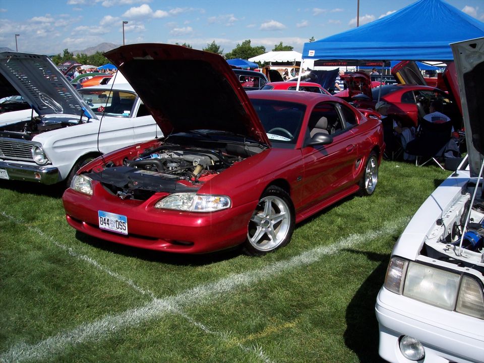 Red Ford Mustang coupe, hood open, showing engine. License plate reads 844 DSS. Parked on grass at car show