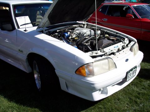 1972 Ford Ranchero - White 1987 Ford Mustang GT 5.0 on display with its engine exposed, parked next to a red vehicle.