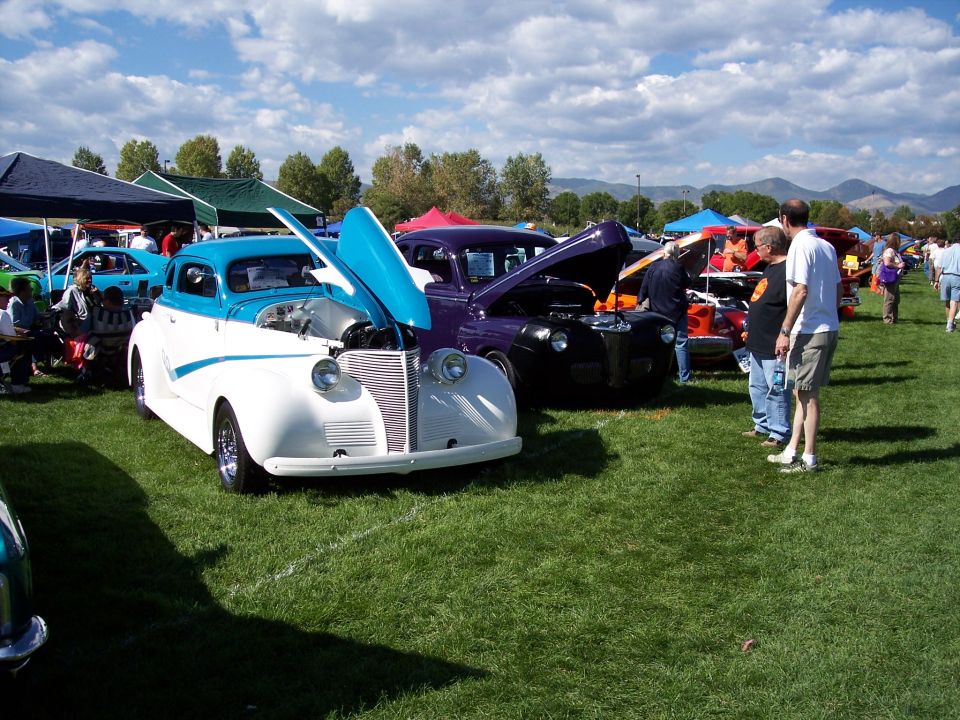 two-tone classic car with hood open, purple classic car behind it, people milling around at an outdoor car show