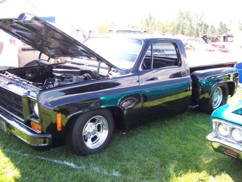 1972 Ford Ranchero - A black pickup truck with its hood open is displayed on a grassy field next to another vehicle.