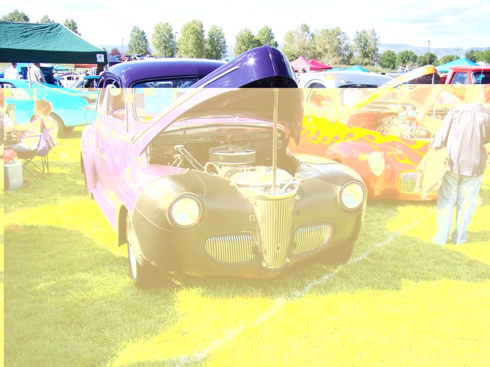 Purple and black vintage car with hood open, showing engine. Another car with flames is behind it