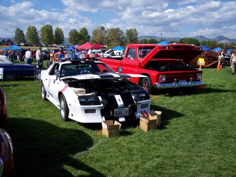 1972 Ford Ranchero - A white police car with its hood open is parked on a grassy field next to a red pickup truck.