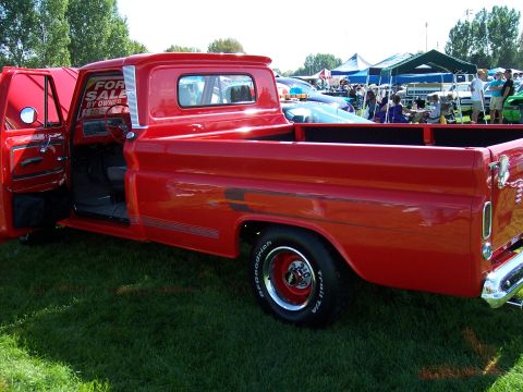 1972 Ford Ranchero - A bright red pickup truck is parked on grass at an outdoor event, with its driver's side door open and a 'For Sale By Owner' sign displayed.
