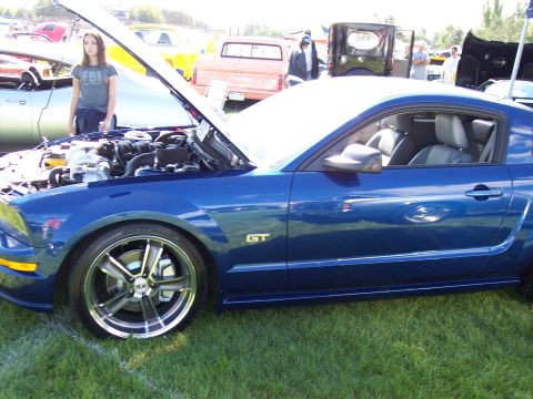 1972 Ford Ranchero - A blue Ford Mustang GT is displayed with its hood open at an outdoor car show, with other vehicles visible in the background.