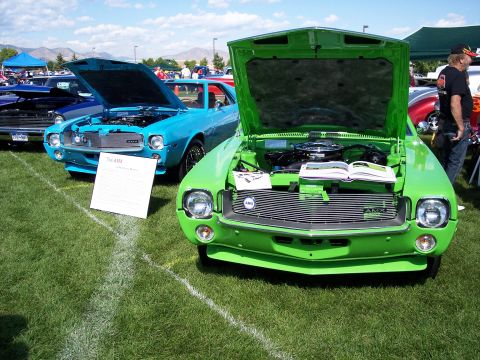 1972 Ford Ranchero - A bright green AMX is displayed with its hood open, alongside a blue AMX at an outdoor car show.