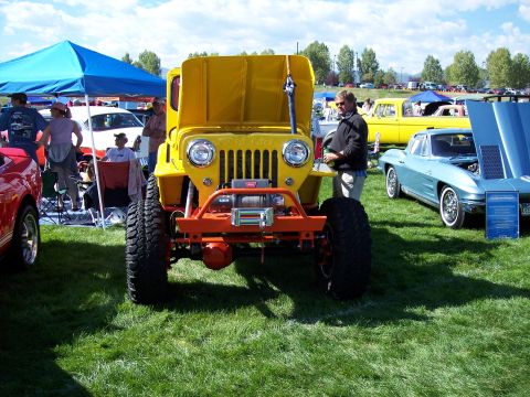 1972 Ford Ranchero - A bright yellow Jeep is displayed at an outdoor car show, with several other vehicles and people around it.
