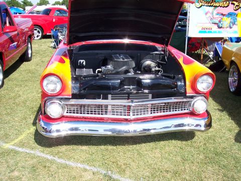 1972 Ford Ranchero - A classic red hot rod with flames and its hood open is displayed on a grassy field at an outdoor event.