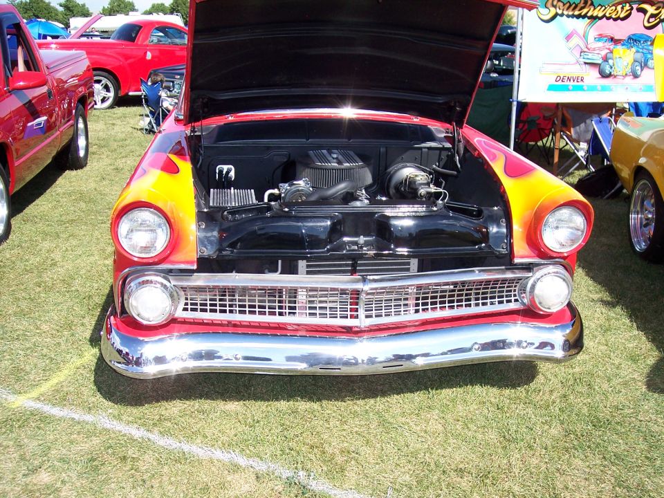 Front view of a red 1955 Ford Fairlane with flames painted on the hood and fenders, engine exposed