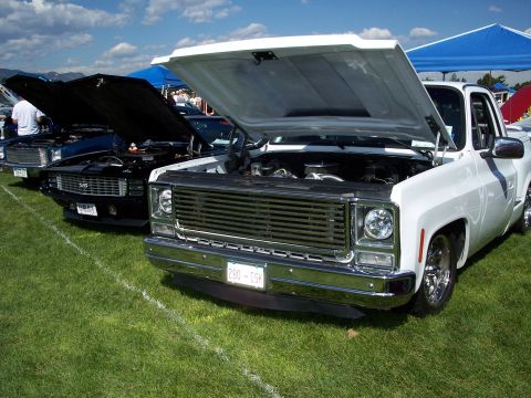 1972 Ford Ranchero - White 1973 Chevrolet C10 pickup truck and a black Chevrolet Camaro at an outdoor car show.