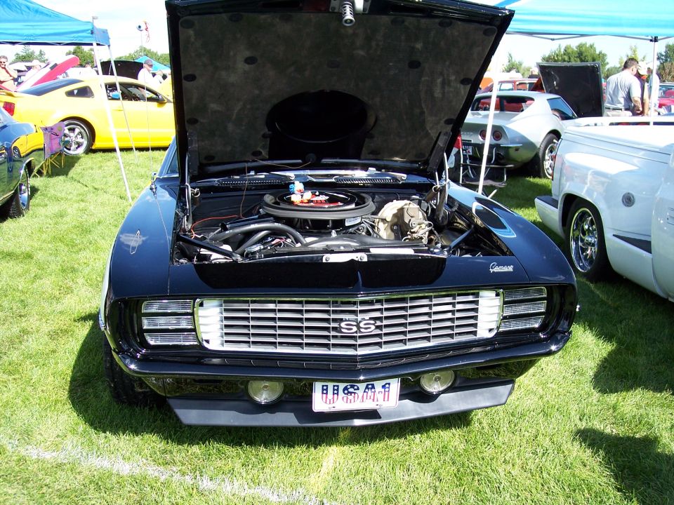 1969 Chevrolet Camaro SS with hood open, showing engine. Yellow car and white truck in background