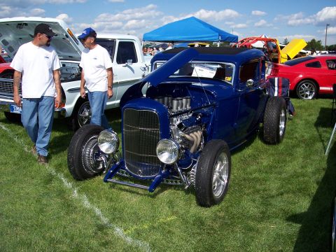 1972 Ford Ranchero - A blue hot rod coupe is displayed on a grassy field with other vehicles present.