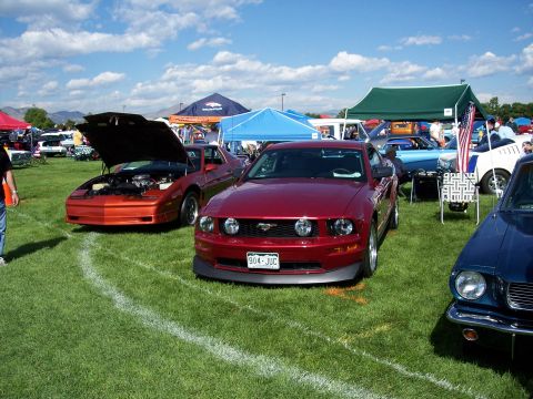 1972 Ford Ranchero - Two cars, a red Ford Mustang and an orange Pontiac Firebird, are displayed on a grassy field under a cloudy sky.