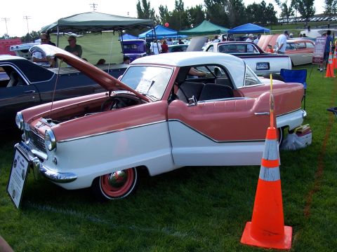 1972 Ford Ranchero - A two-tone pink and white 1957 Nash Metropolitan is displayed with its hood up at an outdoor car show.