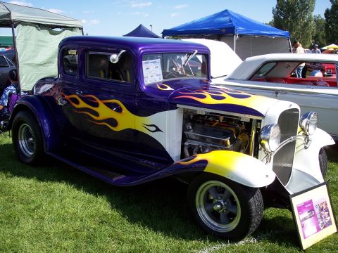 1972 Ford Ranchero - A customized hot rod with flame graphics and an open engine bay is displayed on a grassy field at an outdoor event.