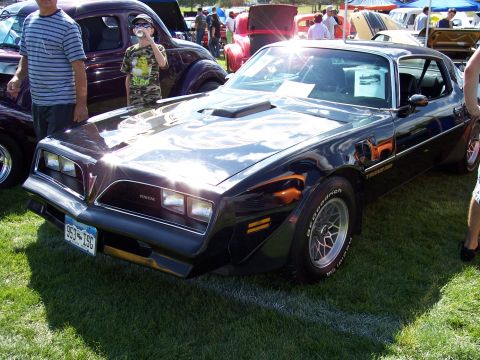 1972 Ford Ranchero - A black Pontiac Firebird Trans Am is parked on grass with other vehicles and people around it at an outdoor car show.