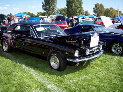 1972 Ford Ranchero - A classic black Ford Mustang is displayed at an outdoor car show with other vehicles and tents in the background.