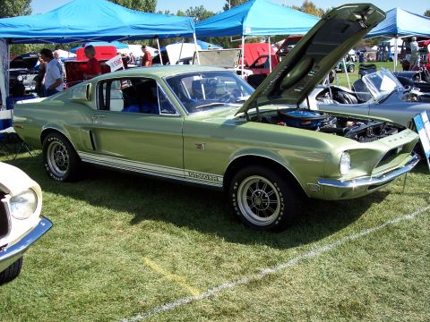 1972 Ford Ranchero - A green 1968 Ford Mustang GT500 KR is displayed with its hood open at a car show, with other vehicles and tents in the background.