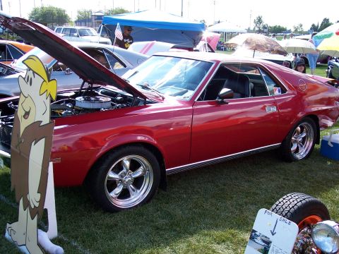 1972 Ford Ranchero - A red coupe, possibly a 1970 AMC AMX, is displayed with its hood open at an outdoor car show.