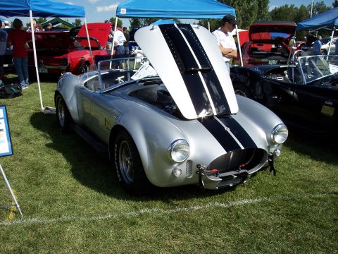 1972 Ford Ranchero - A silver Shelby Cobra with black racing stripes is displayed with its hood open at an outdoor car show.