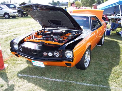1972 Ford Ranchero - An orange and black AMC AMX is displayed with its hood open, showing the engine, at an outdoor car show.