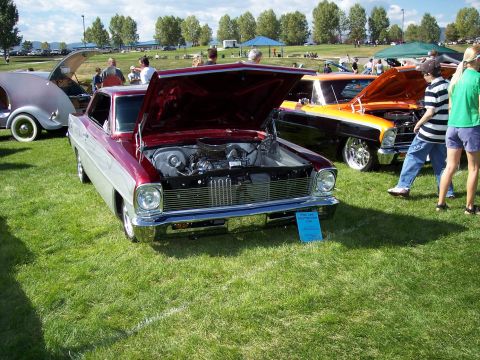 1972 Ford Ranchero - A classic car show features several vehicles on display, with one maroon and silver car prominently displayed with its hood open.