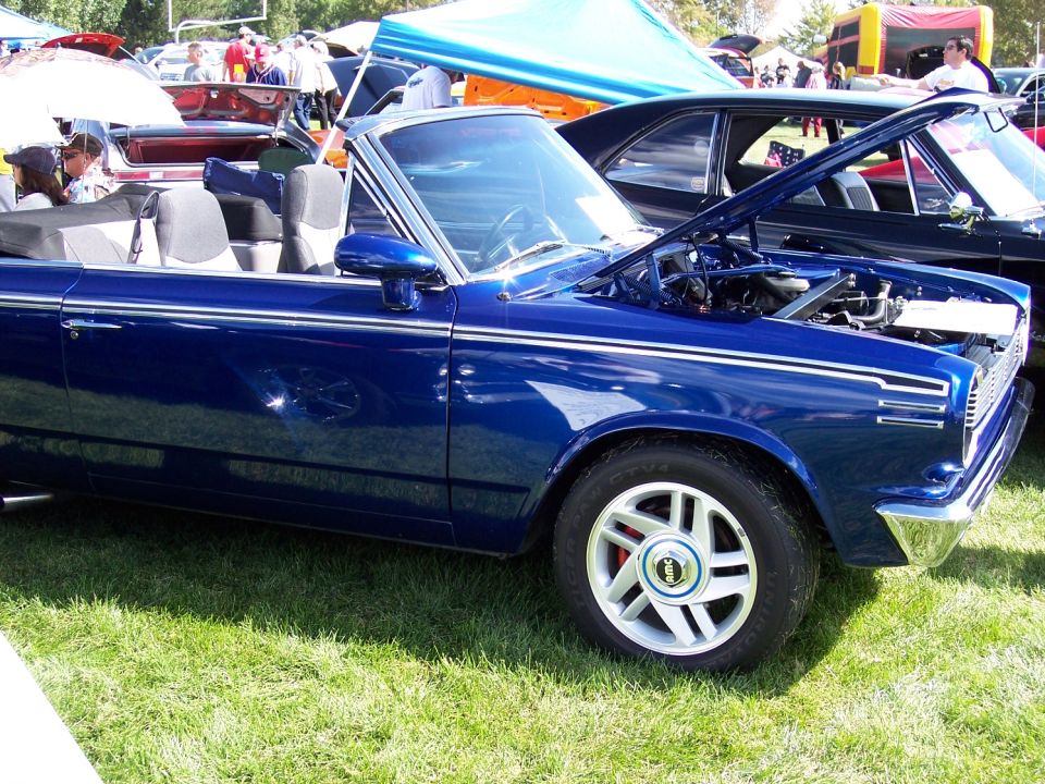 Blue convertible parked on grass, hood open showing engine. Another car is parked next to it