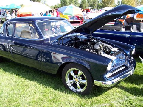 1972 Ford Ranchero - A dark blue 1955 Studebaker President is displayed with its hood open, revealing the engine, at an outdoor car show.