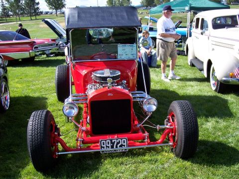 1972 Ford Ranchero - A red hot rod with a black soft top and exposed engine is parked on grass at an outdoor event.