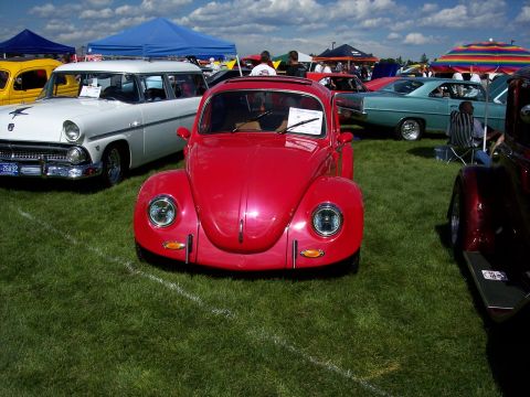 1972 Ford Ranchero - A bright red Volkswagen Beetle is parked on a grassy field at an outdoor car show, with other vehicles visible in the background.