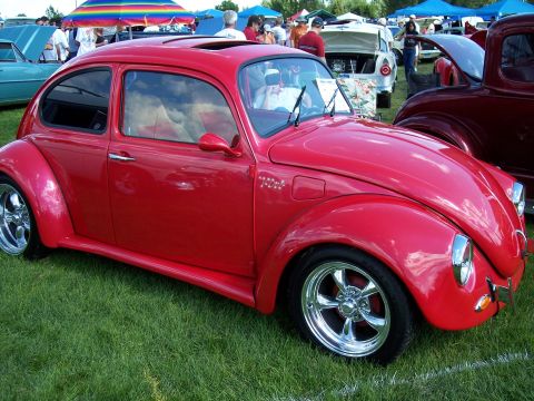 1972 Ford Ranchero - A red Volkswagen Beetle is displayed on a grassy field with other vehicles and tents in the background.