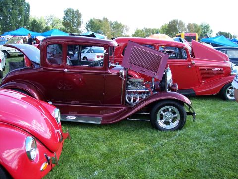 1972 Ford Ranchero - A maroon 1930s coupe, possibly a Ford Model A, is displayed with its hood open, revealing a custom engine, next to a red Volkswagen Beetle.