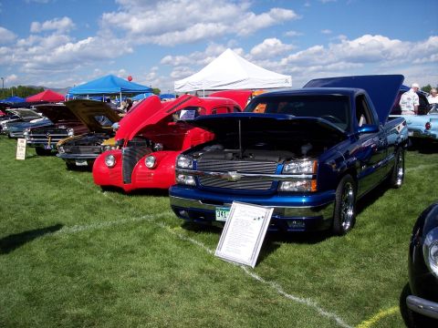 1972 Ford Ranchero - A blue pickup truck is displayed with its hood open at an outdoor car show, alongside other vehicles.