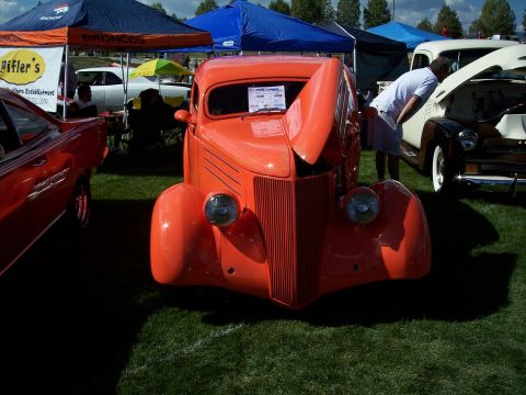 1972 Ford Ranchero - A vintage orange coupe is displayed at an outdoor car show with other vehicles and tents in the background.