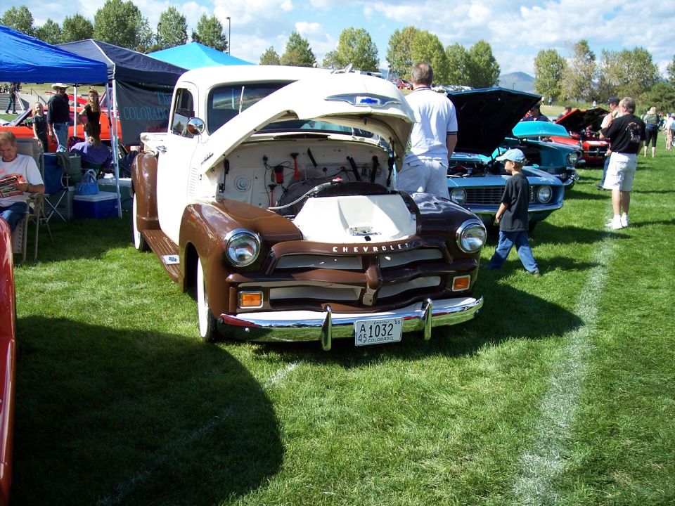 Brown and white 1950 Chevrolet pickup truck with hood open, parked on grass at car show. License plate A1032