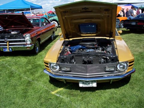 1972 Ford Ranchero - Two classic cars are displayed on a grassy field under tents at an outdoor car show.
