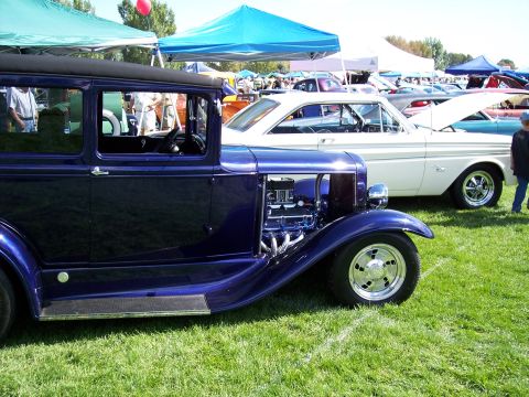 1972 Ford Ranchero - A custom hot rod sedan is displayed at an outdoor car show, with other vehicles and tents in the background.