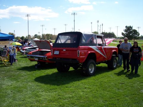 1972 Ford Ranchero - A red 1972 Ford Bronco with a soft top is displayed at an outdoor car show next to another vehicle.