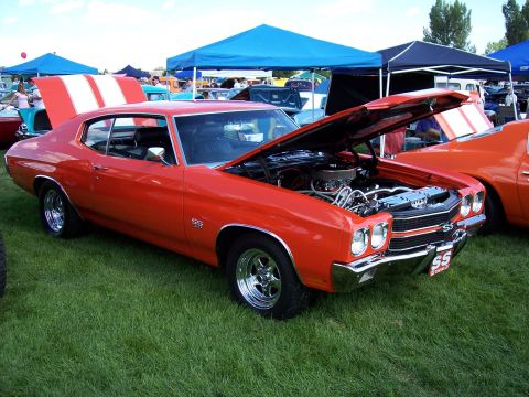 1972 Ford Ranchero - A bright orange muscle car with racing stripes on the trunk is displayed at an outdoor car show.