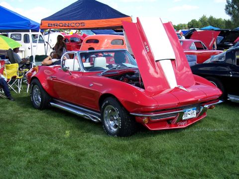 1972 Ford Ranchero - A red convertible sports car is parked on grass at an outdoor event with other vehicles and tents in the background.