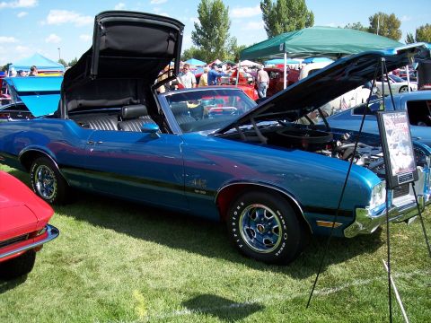 1972 Ford Ranchero - A blue 1972 Oldsmobile Cutlass Supreme convertible is displayed with its top up and hood open at a car show.